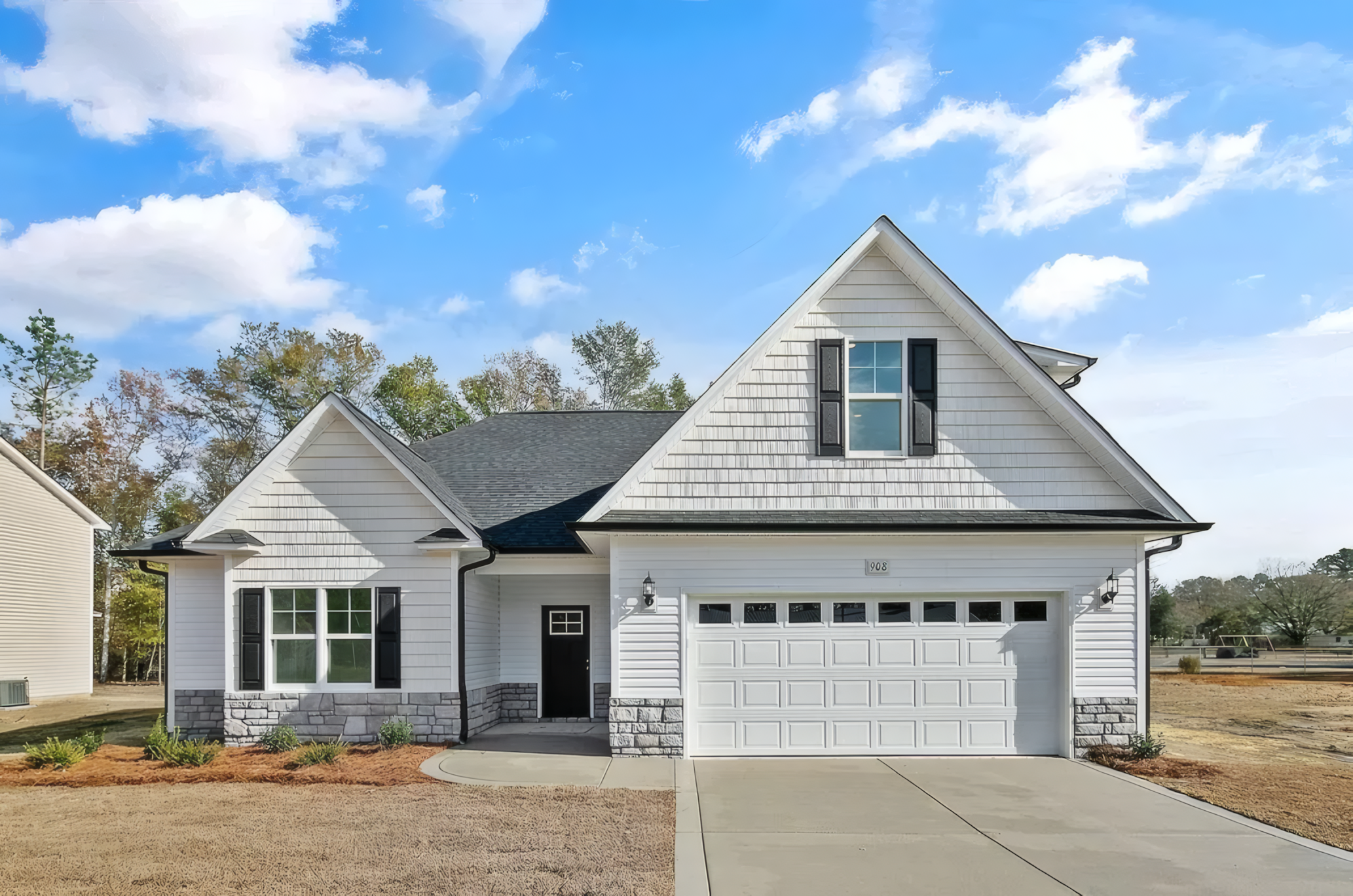 White house with large white garage. The roof is dark greyish blue and the bottom of the house is outlined with stone pattern