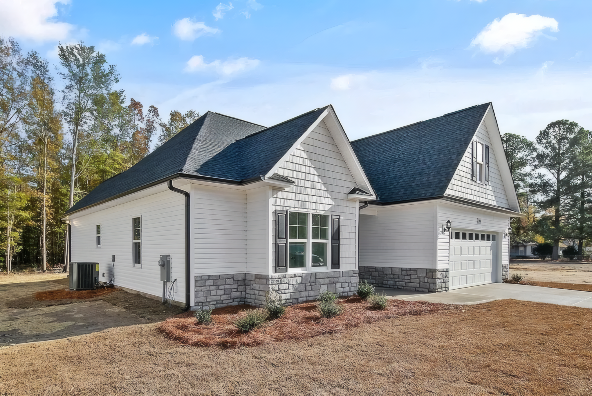 Side shot of white house with large white garage. The roof is dark greyish blue and the bottom of the house is outlined with stone pattern